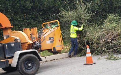 A man is standing next to a tree chipper on the side of the road.