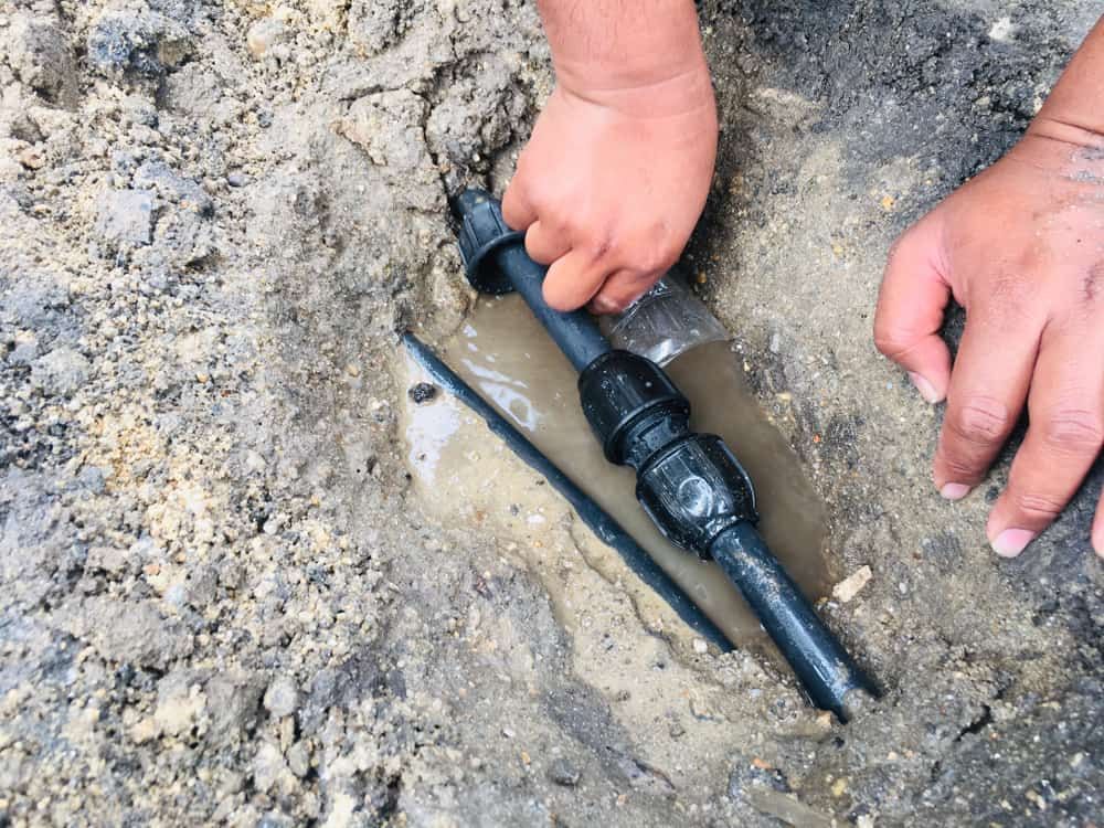 A Person Is Fixing a Broken Pipe in The Dirt — Origin Plumbing & Gas in Tuckurimba, NSW