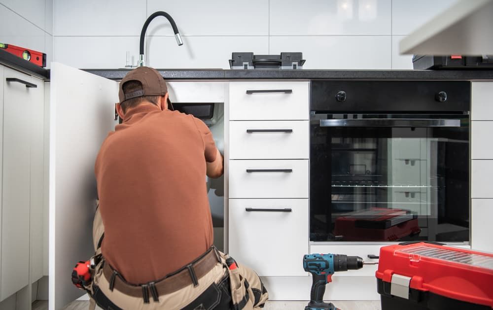 A Man Is Fixing a Sink in A Kitchen — Origin Plumbing & Gas in Tuckurimba, NSW