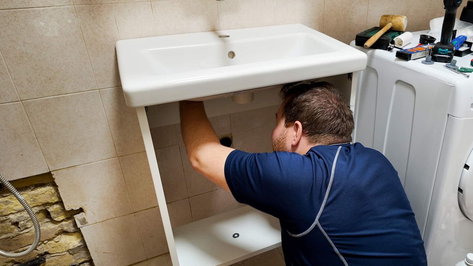 A Man Is Fixing a Sink in A Bathroom — Origin Plumbing & Gas in Lismore, NSW