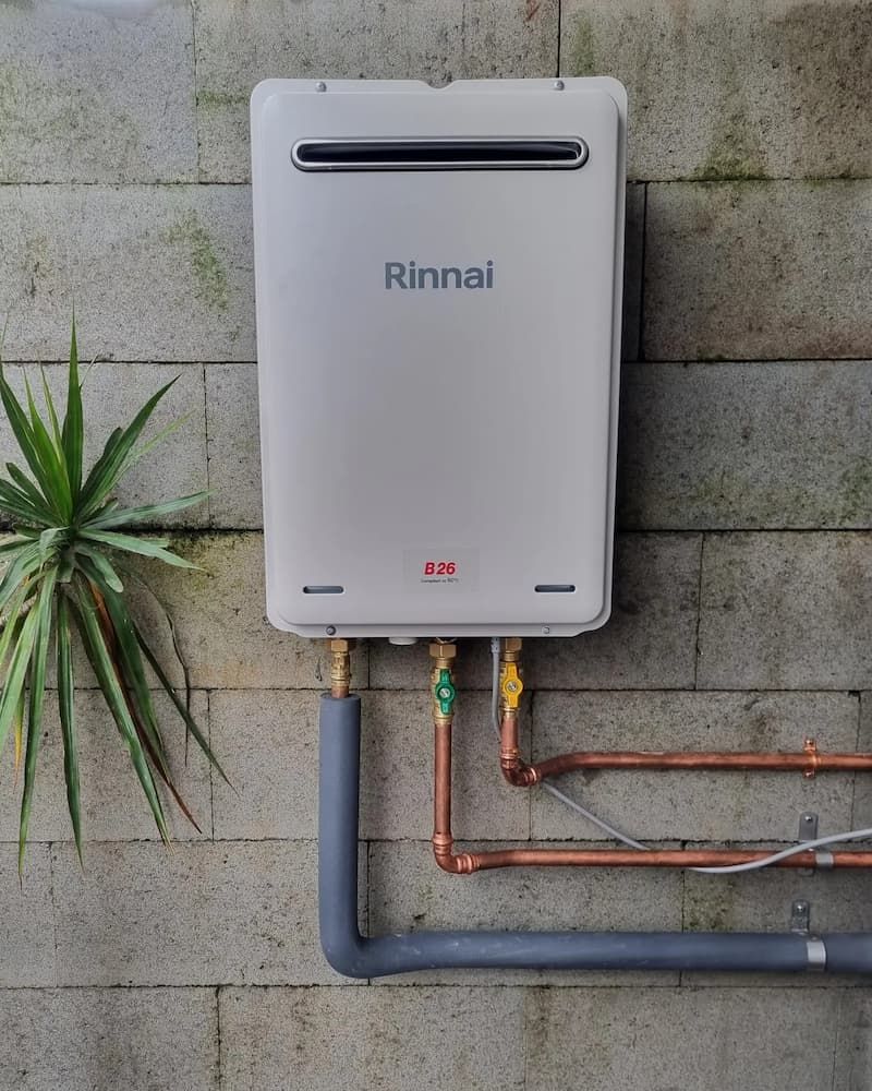 A Rinnai Water Heater Is Attached to A Brick Wall — Origin Plumbing & Gas in Tuckurimba, NSW