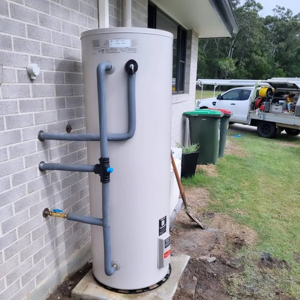 A White Water Heater Is Sitting on The Side of A Brick Building — Origin Plumbing & Gas in Brunswick Heads, NSW