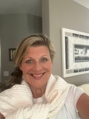 Smiling person in a white sweater taking a selfie indoors, with framed wall art behind them.