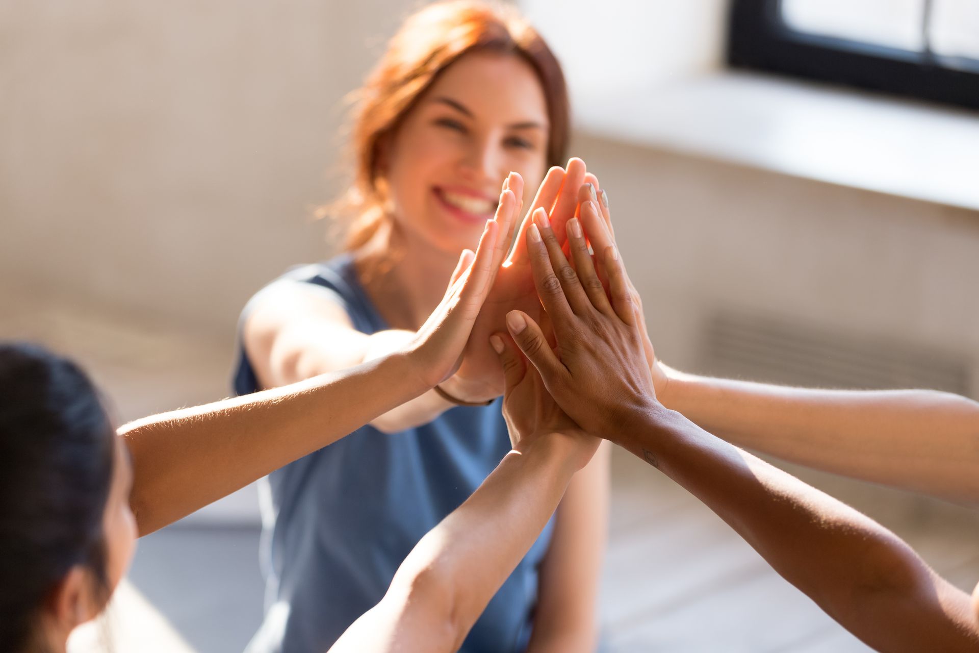Hands meeting in a high-five, with a smiling person blurred in the background indoors.