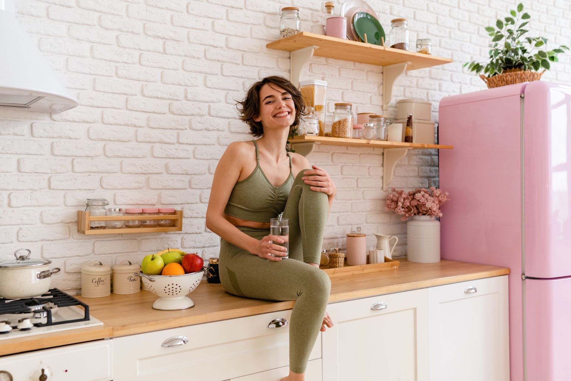Woman sitting on a kitchen counter in a bright, modern kitchen beside a pink refrigerator