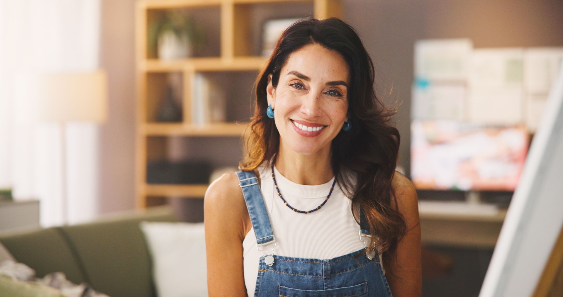 Smiling woman in denim overalls seated at a desk in a bright office