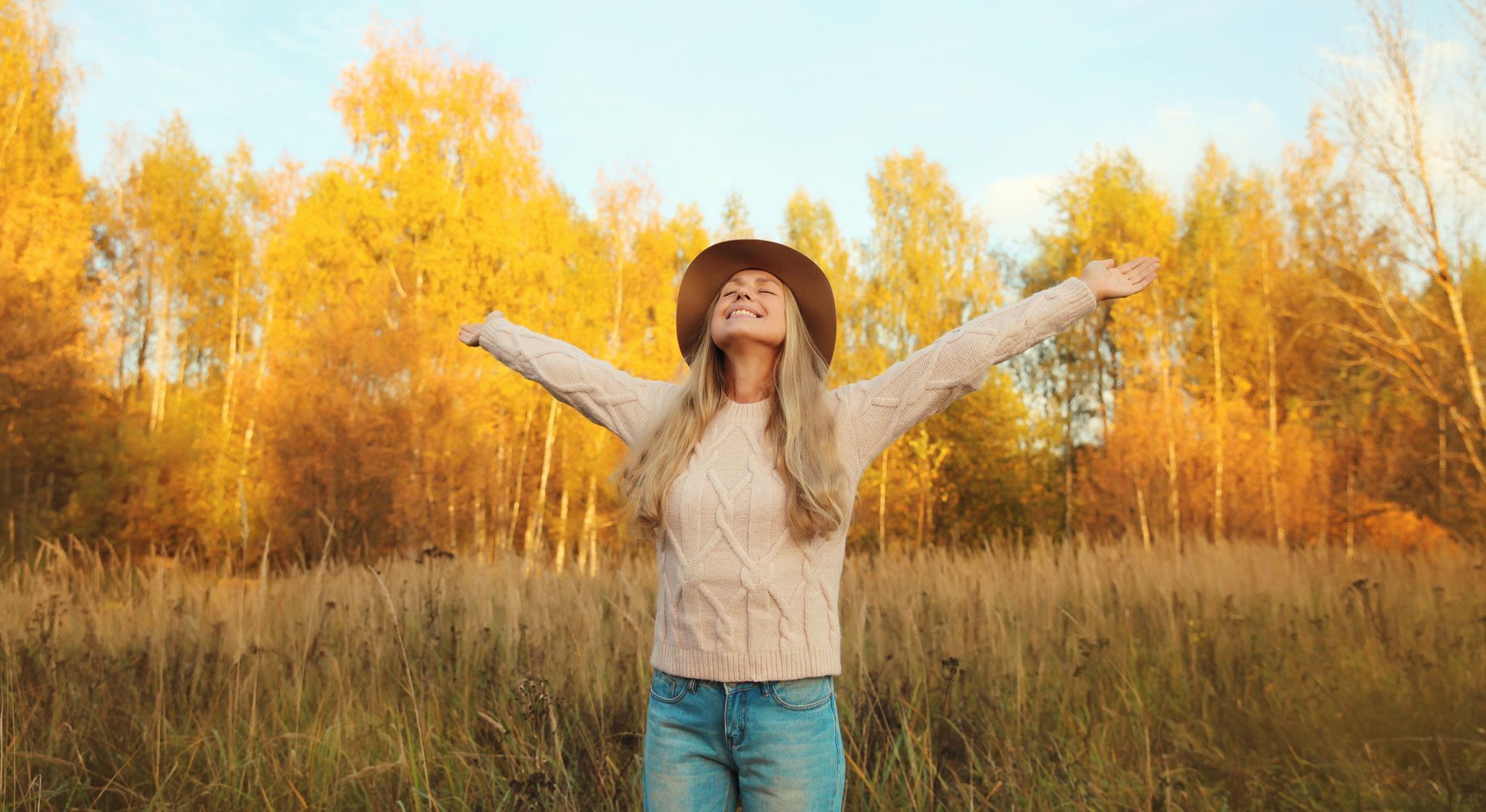 Person standing in a golden autumn field with arms raised under bright sunlight