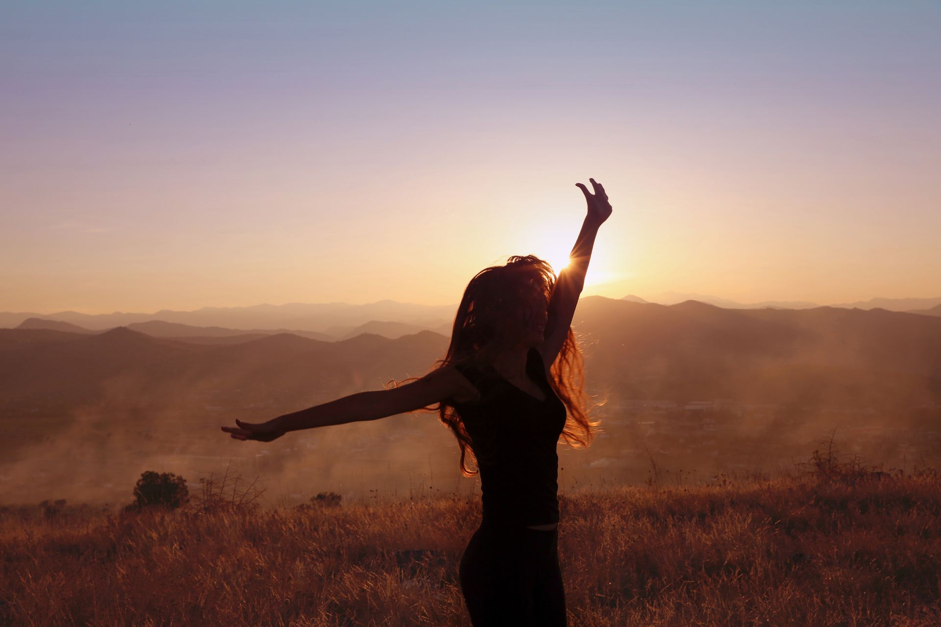 Silhouette of a person with arms raised in a sunset field, backlit by golden light