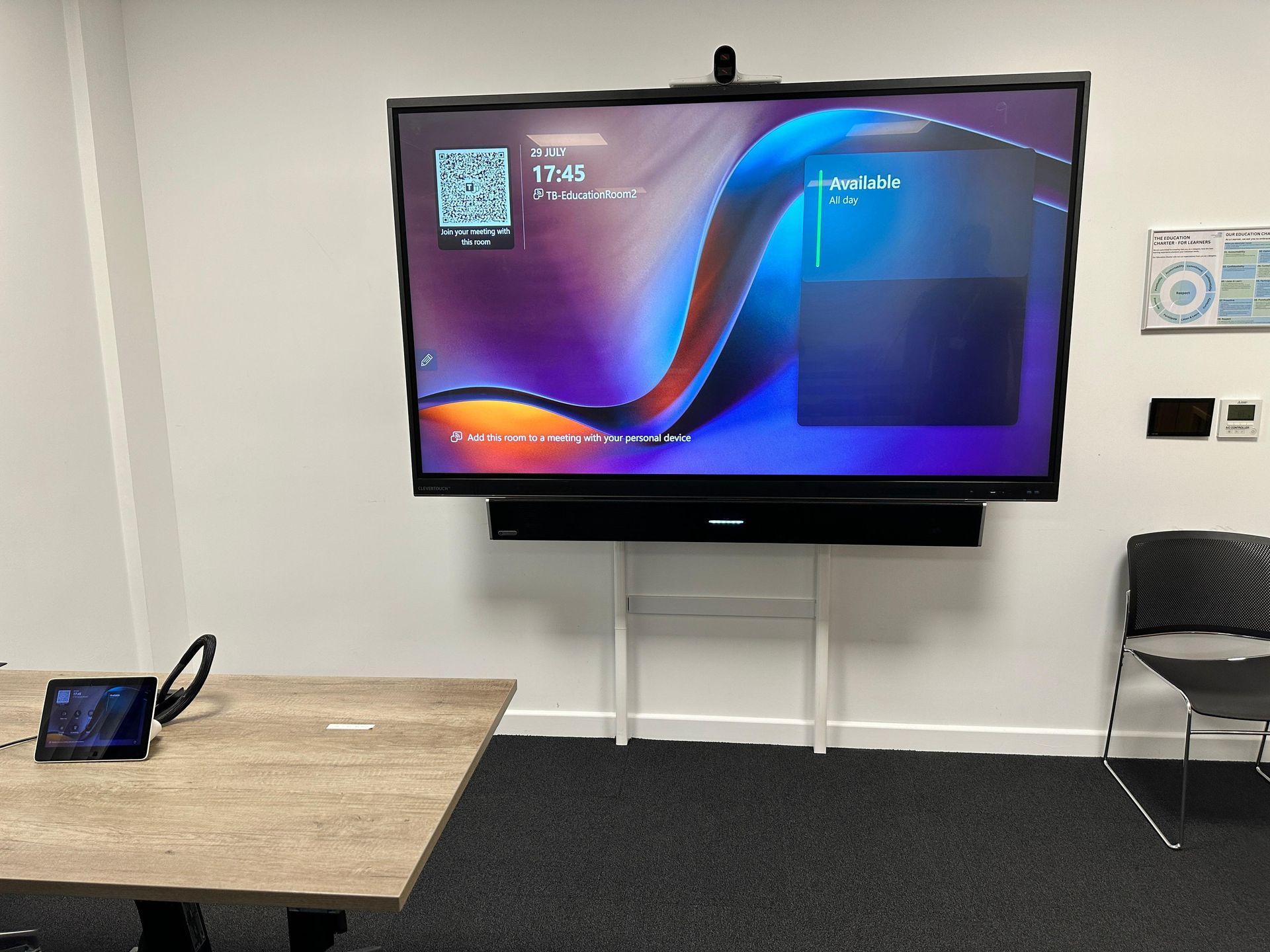 Meeting room with a wall-mounted video conferencing display, soundbar and tabletop controller