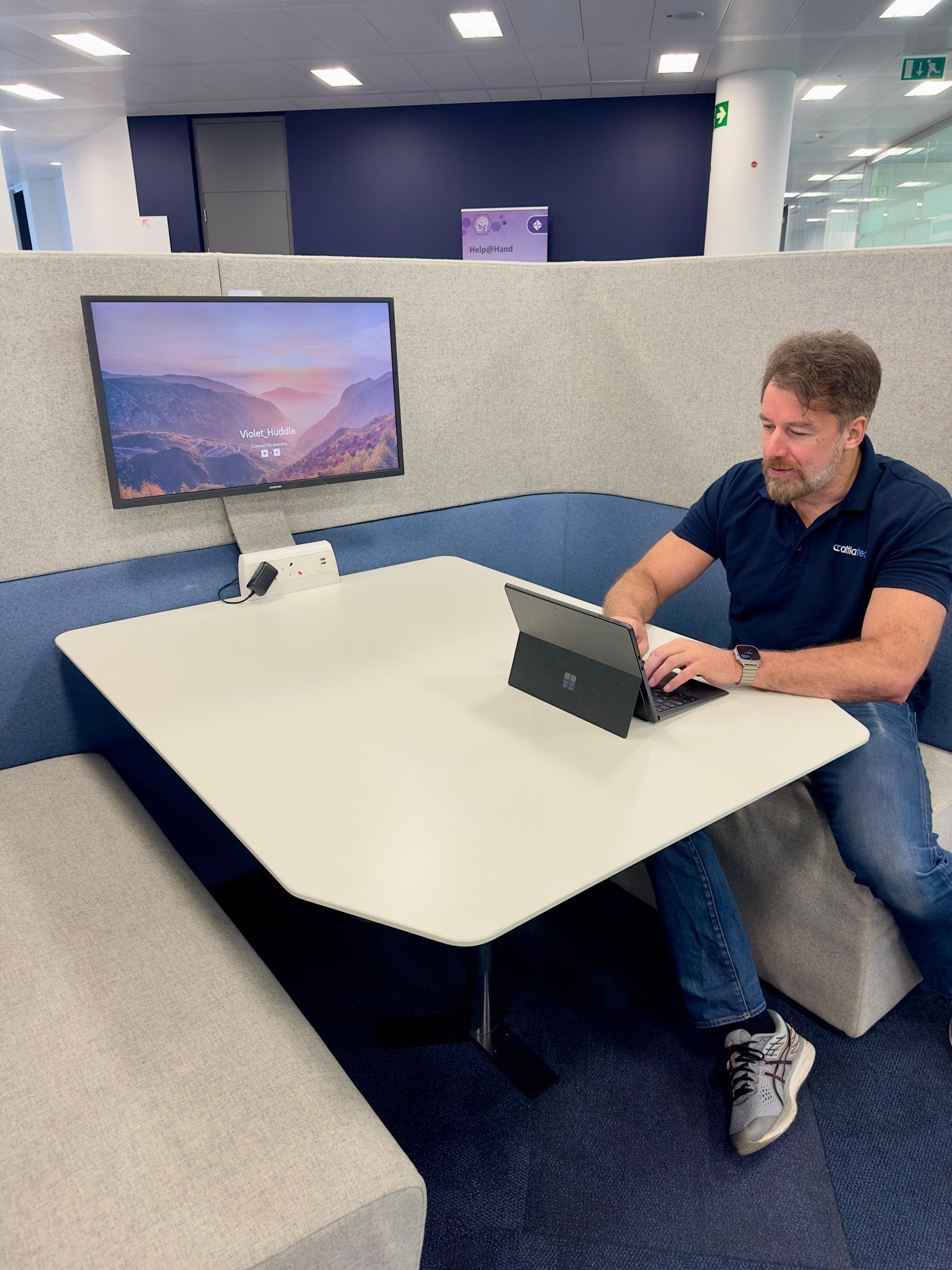 Workplace collaboration booth with a wall-mounted display and a user working at a laptop
