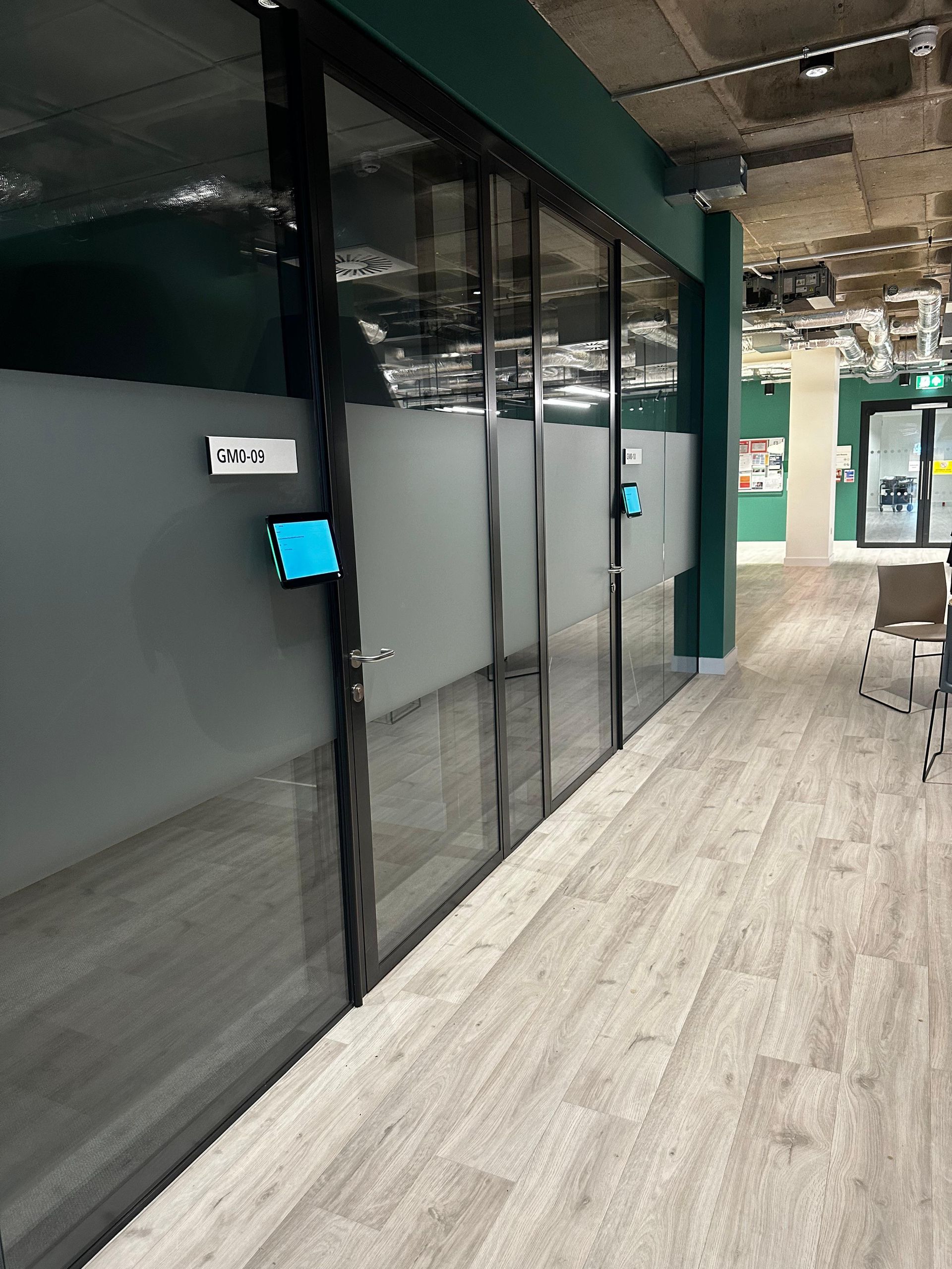 Office corridor with glass meeting rooms and a wall-mounted room booking panel