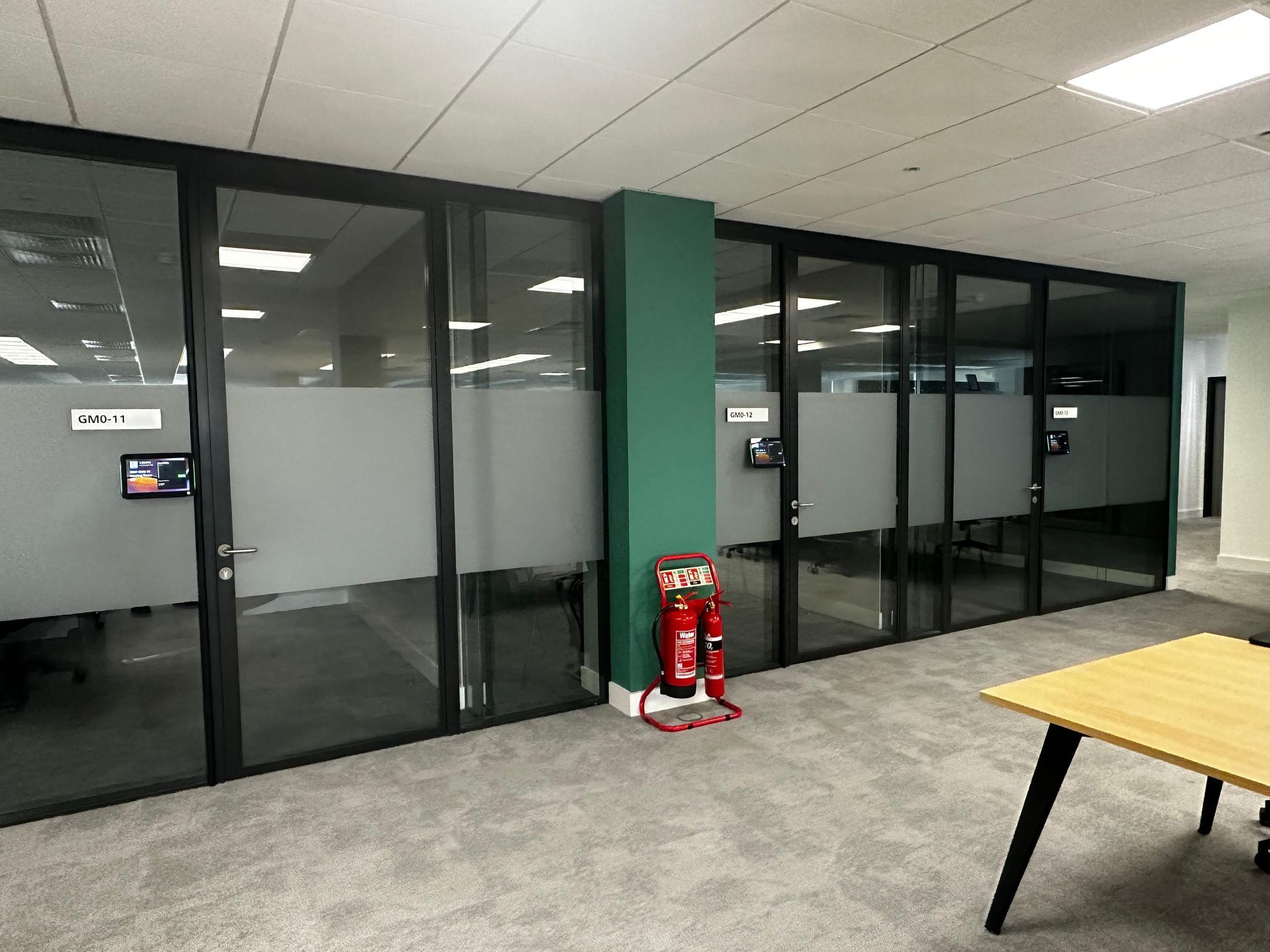 Glass-fronted meeting rooms with wall-mounted room booking panels