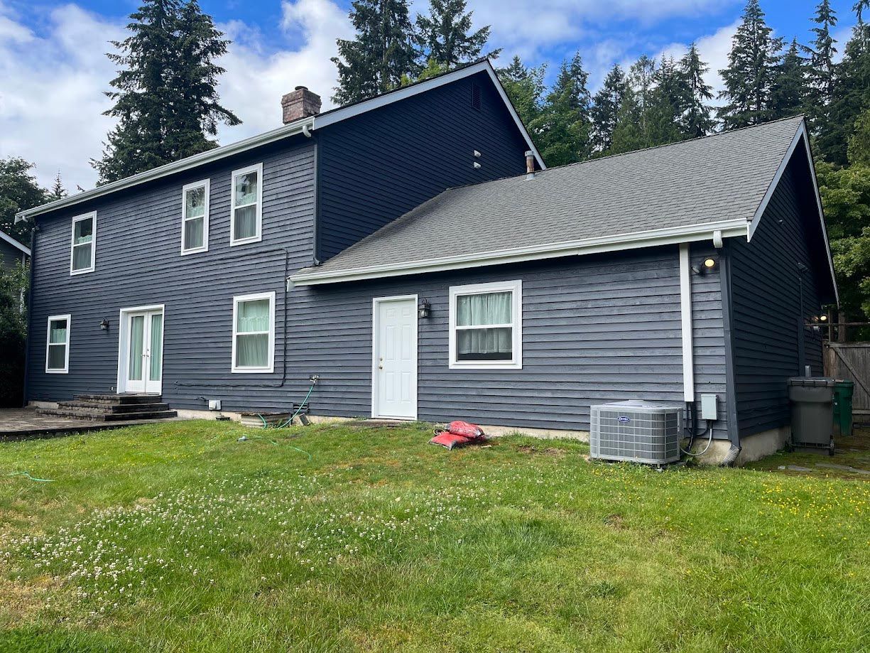 A large gray house with a gray roof is sitting on top of a lush green field.