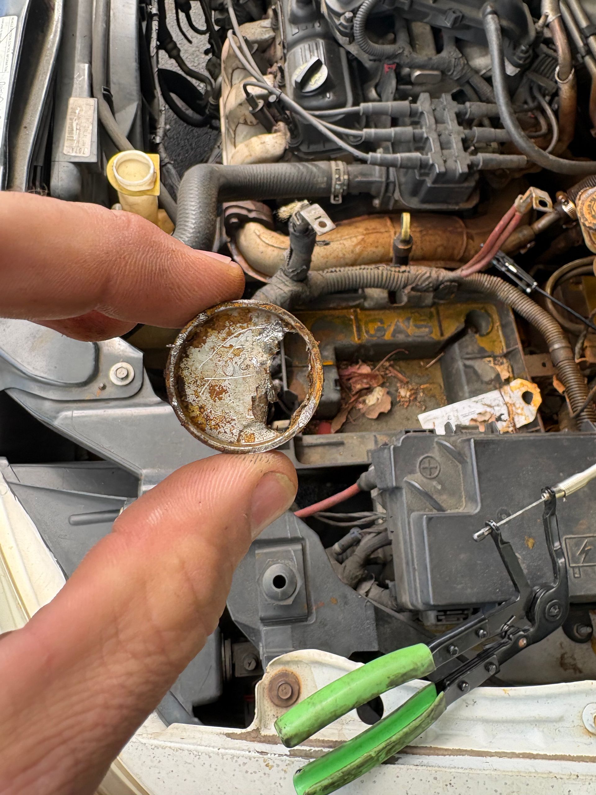 Close-up of a hand holding a clogged, crusty car part inside an engine bay.