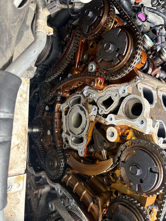 Close-up of a dirty engine timing area with oily chains, gears, and exposed metal parts.