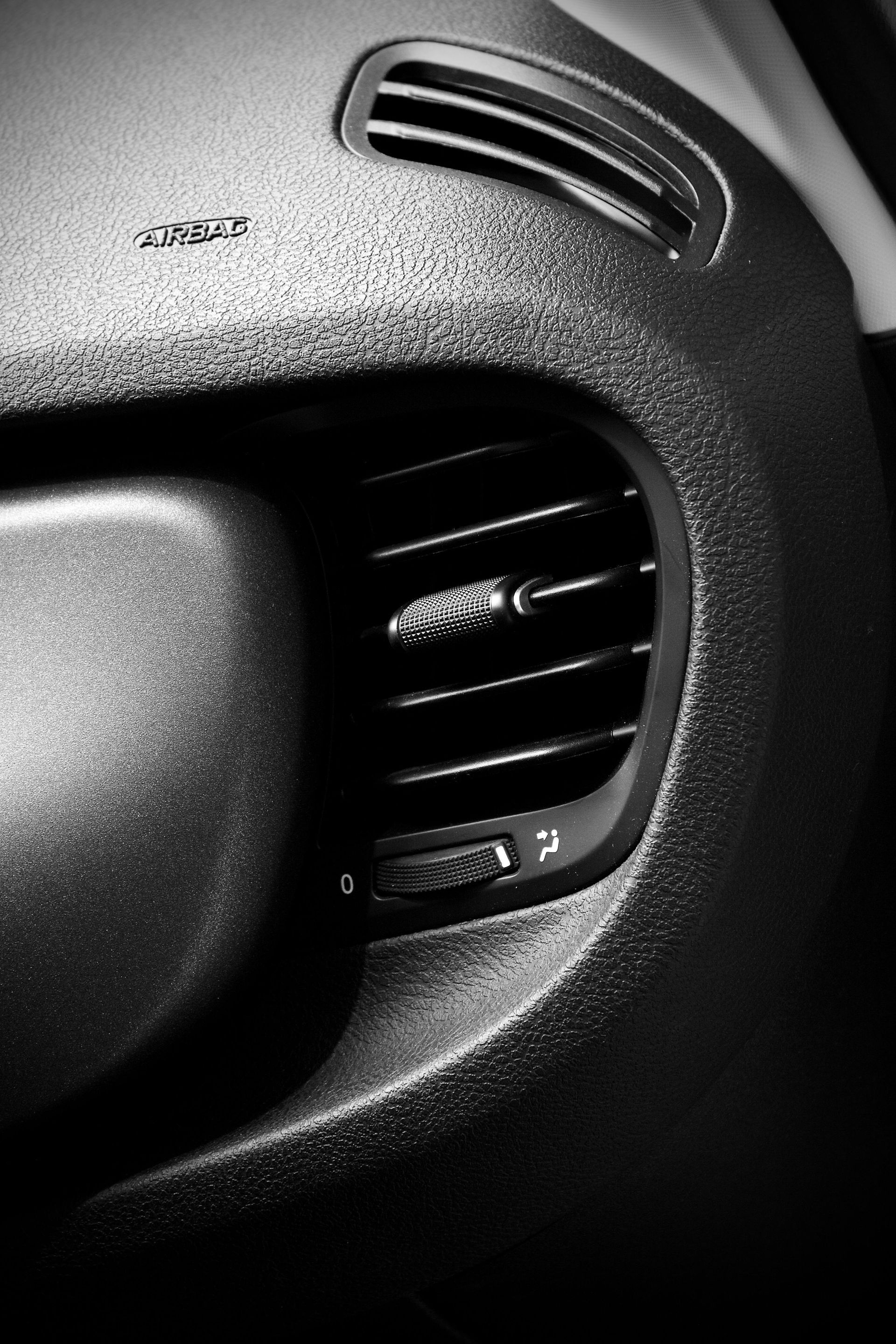 Close-up of a car dashboard air vent with a textured black plastic panel and silver trim