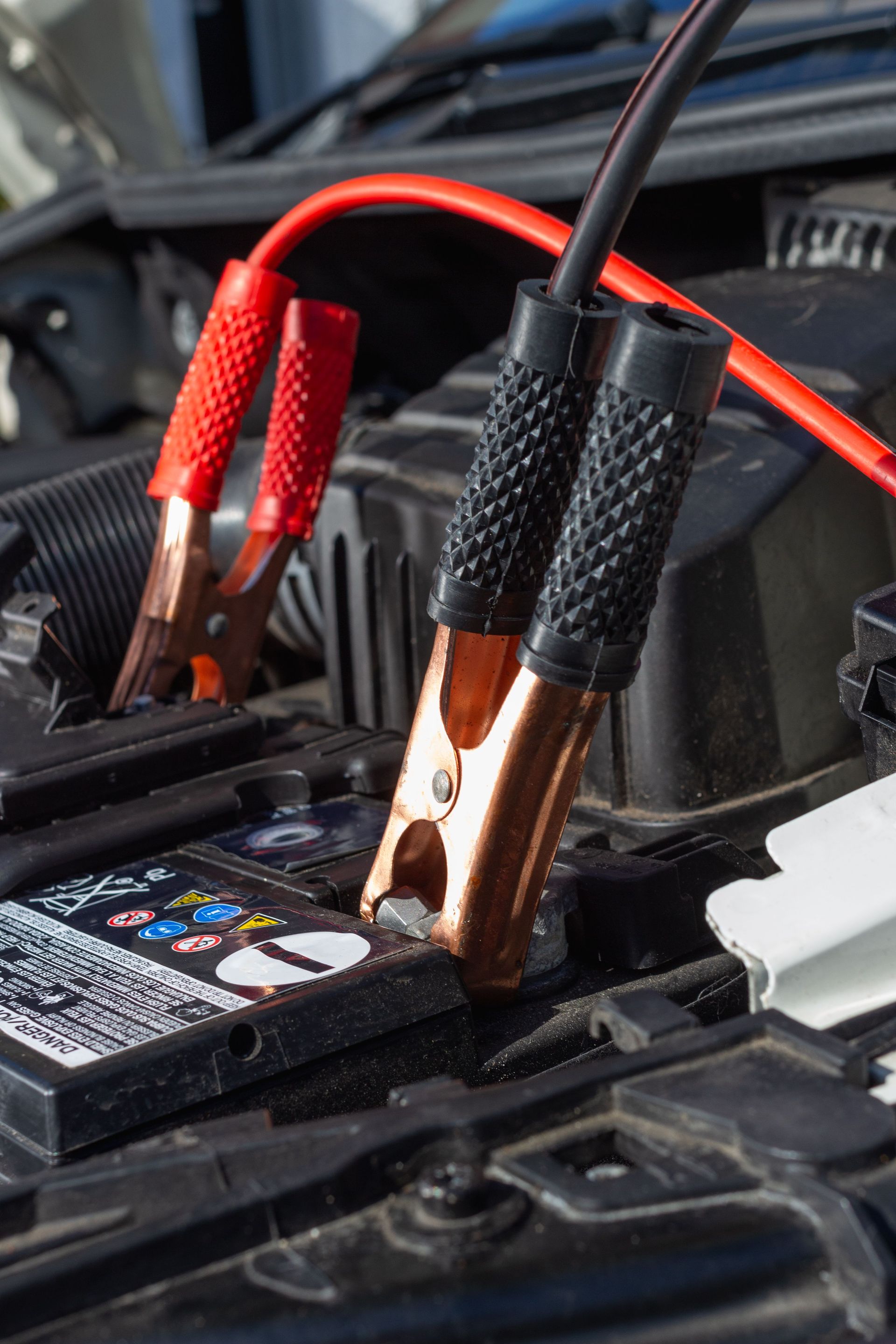Battery being jump-started with red and black alligator clips connected to the terminals.