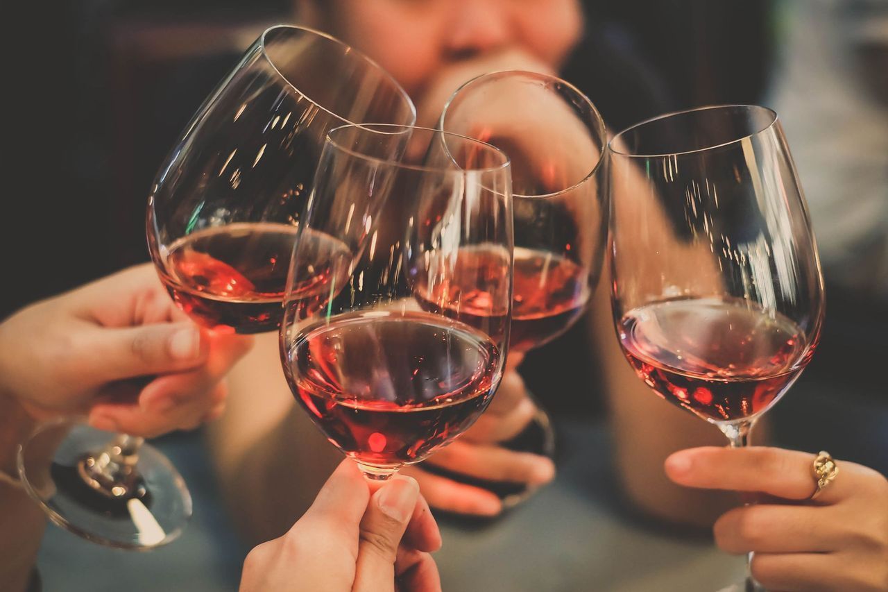 Hands clinking wine glasses filled with red wine, toasting, indoors.