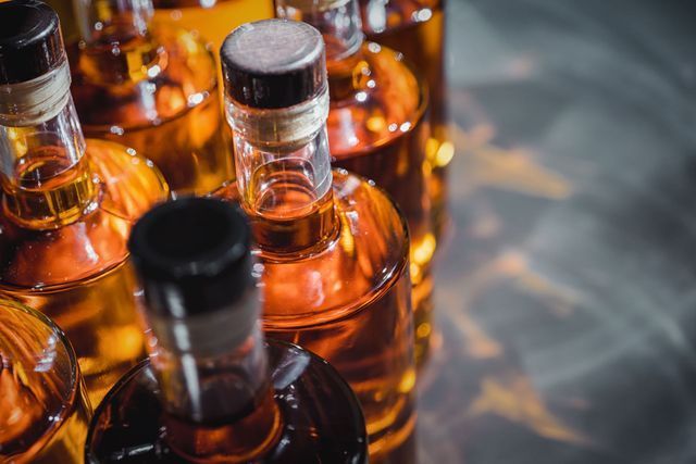 Bottles of amber liquid, tightly packed together, lit by side light.