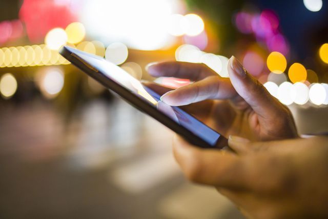 Hand using a smartphone, blurred lights in the background.
