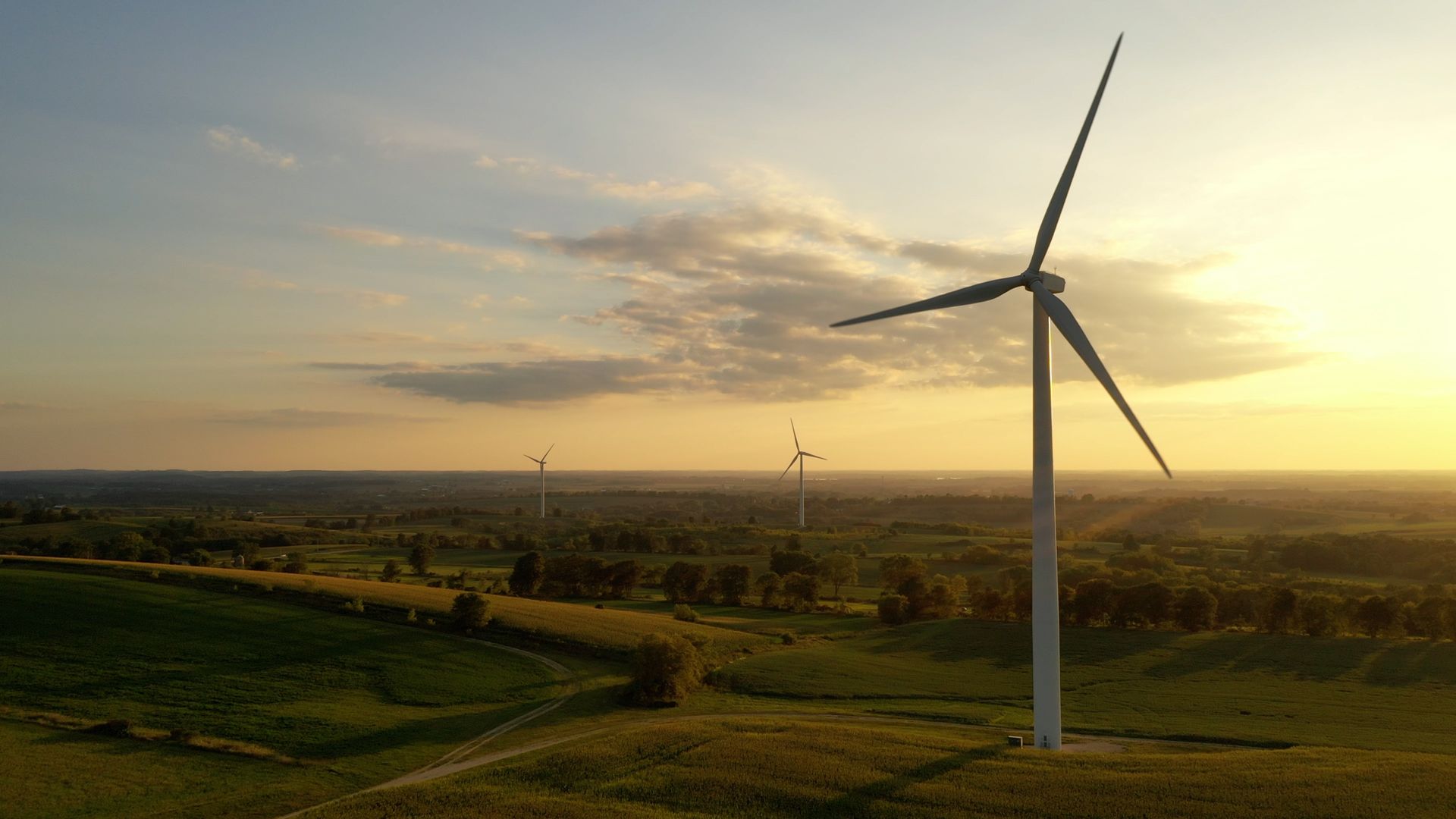Wind turbine on a grassy hill with others in the background, set against a sunset sky.