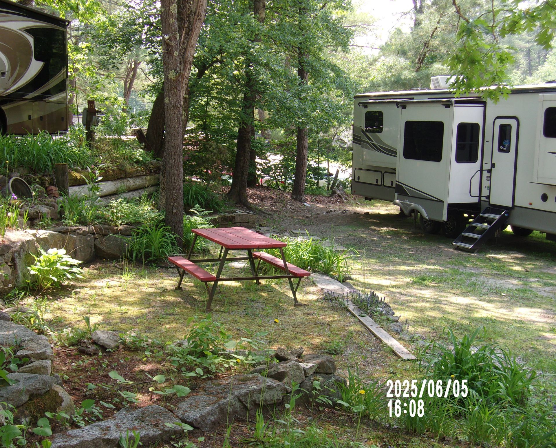 Wooded campsite with a red picnic table beside a white RV and trees in dappled shade