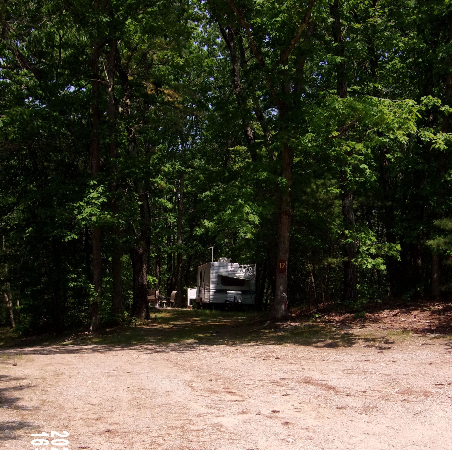RV parked in a shaded wooded clearing beside a dirt area