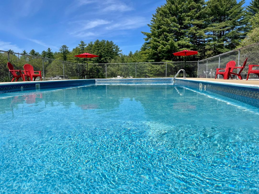 Outdoor swimming pool with clear blue water, red chairs, and umbrellas under a bright sky