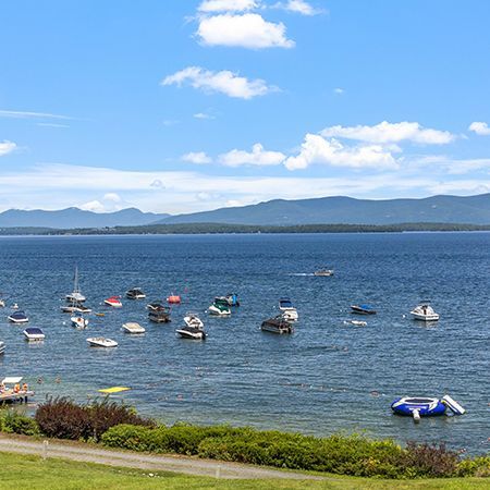 Boats anchored on a calm blue bay with mountains under a bright sky