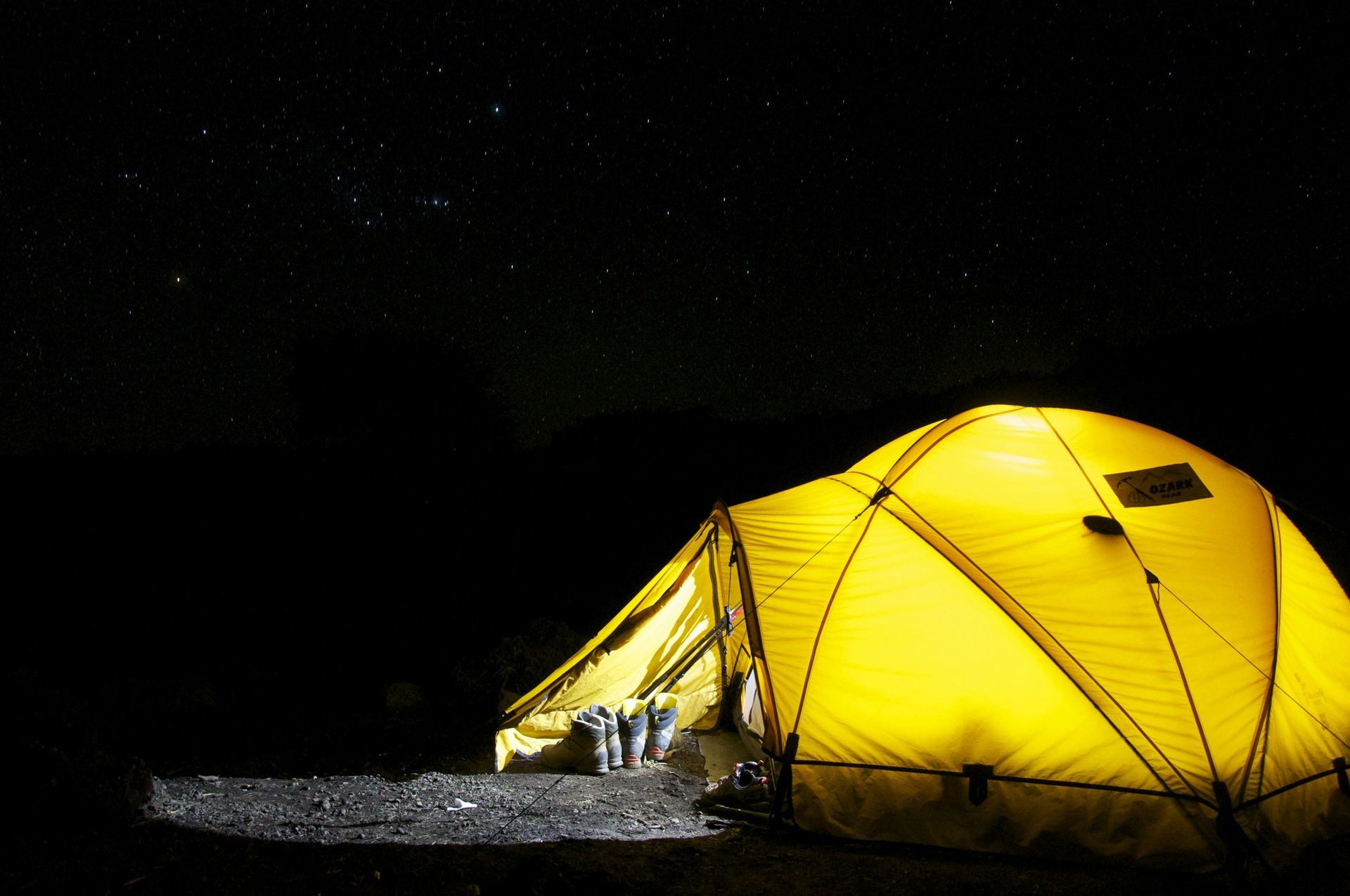 Yellow tent lit at night in a dark campsite under a starry sky