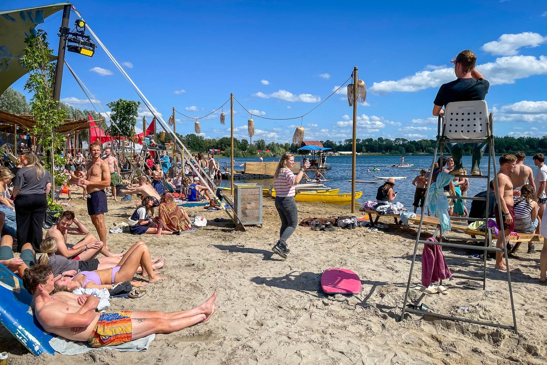 Een groep mensen zit op een strand bij een waterpartij.