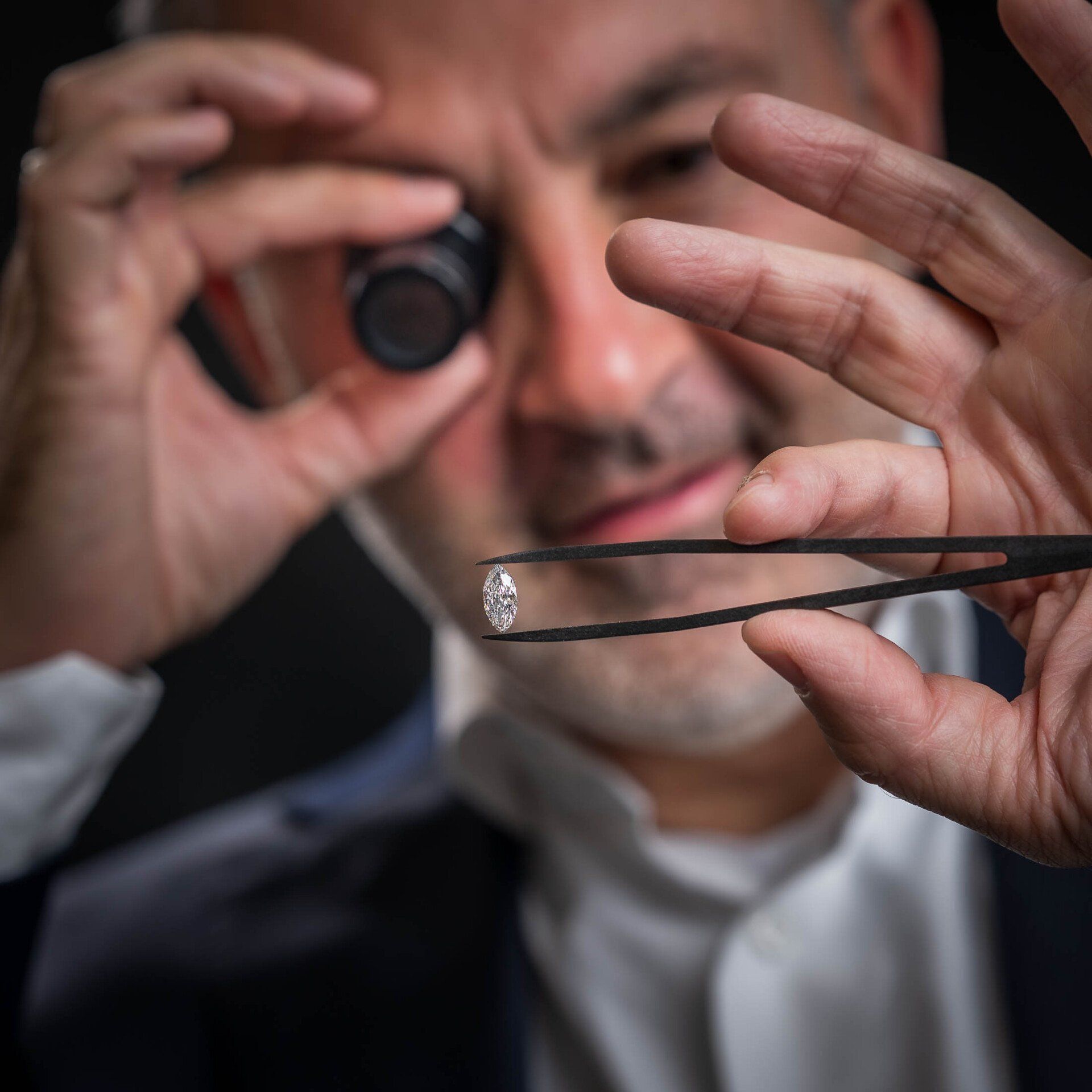 Een man houdt een diamant vast met een pincet en kijkt door een vergrootglas