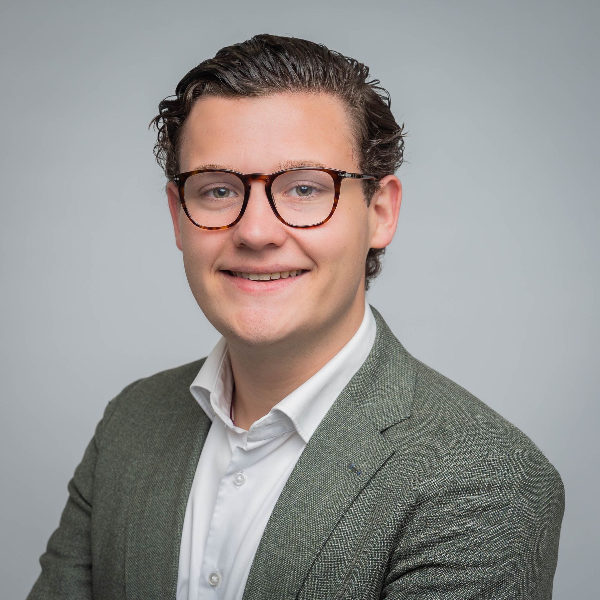 Een man met een bril en een groen jasje lacht naar de camera.