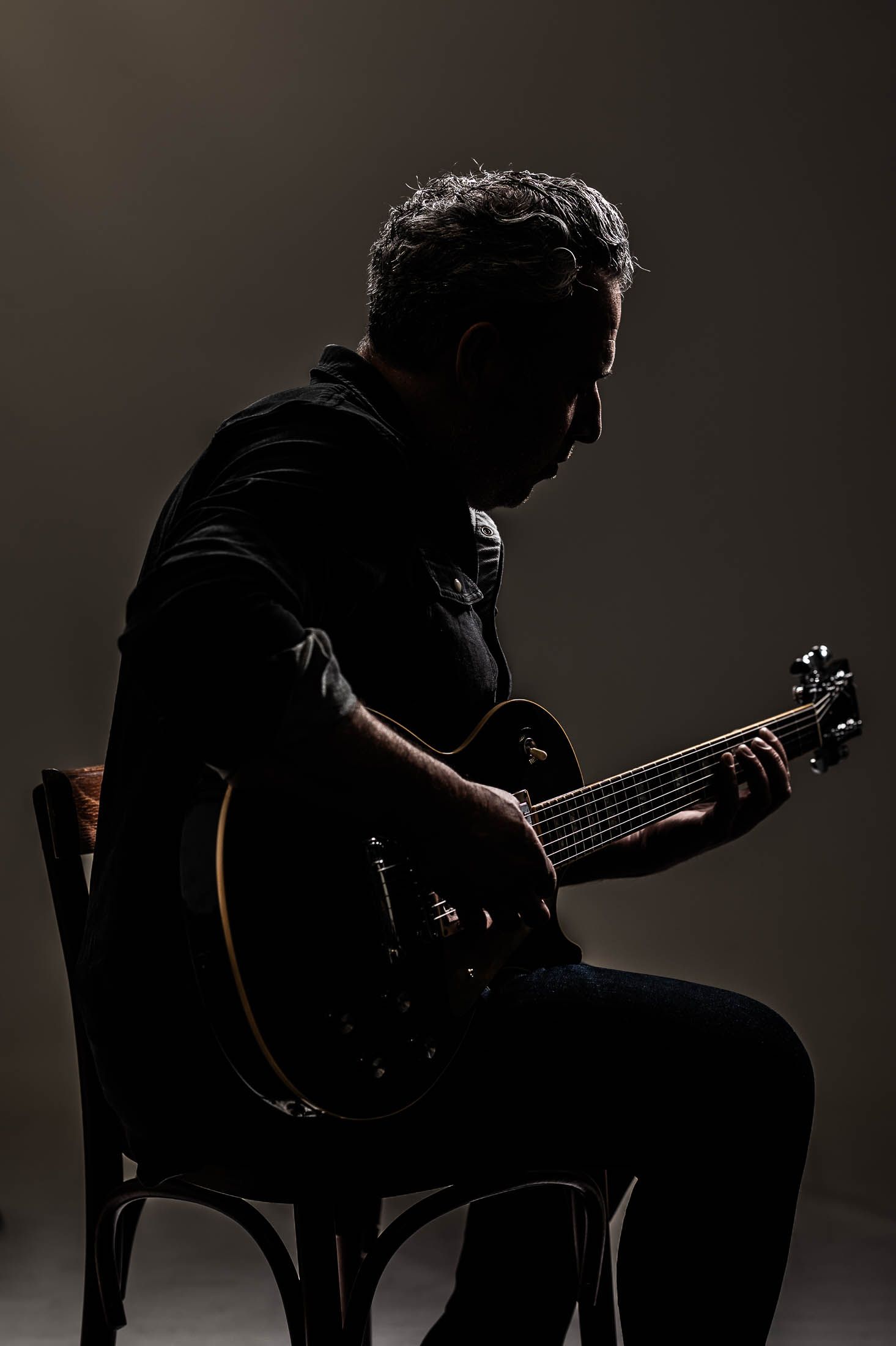 Een man zit op een stoel en bespeelt een elektrische gitaar.