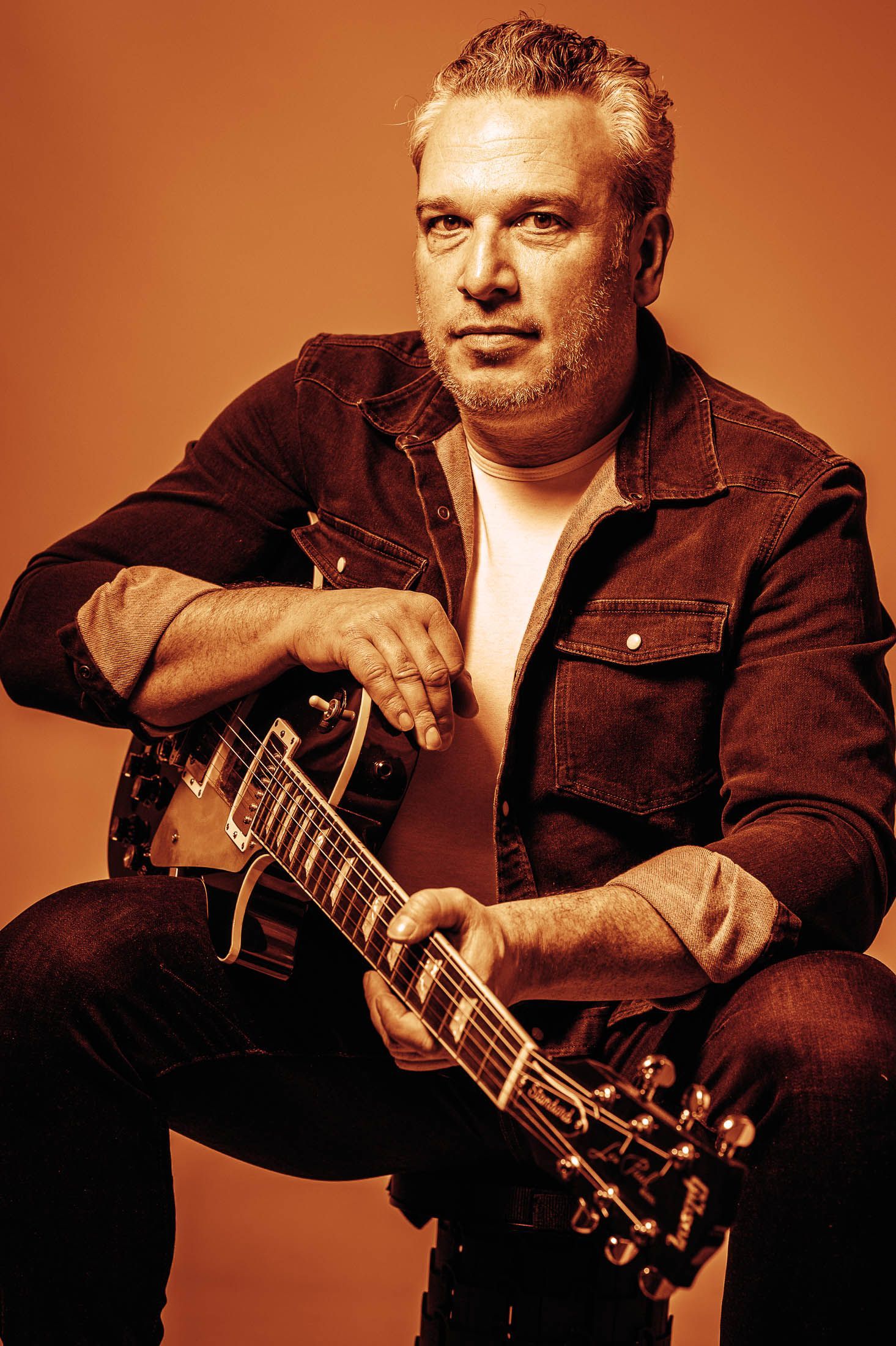 Een man zit op een stoel en houdt een gitaar vast.