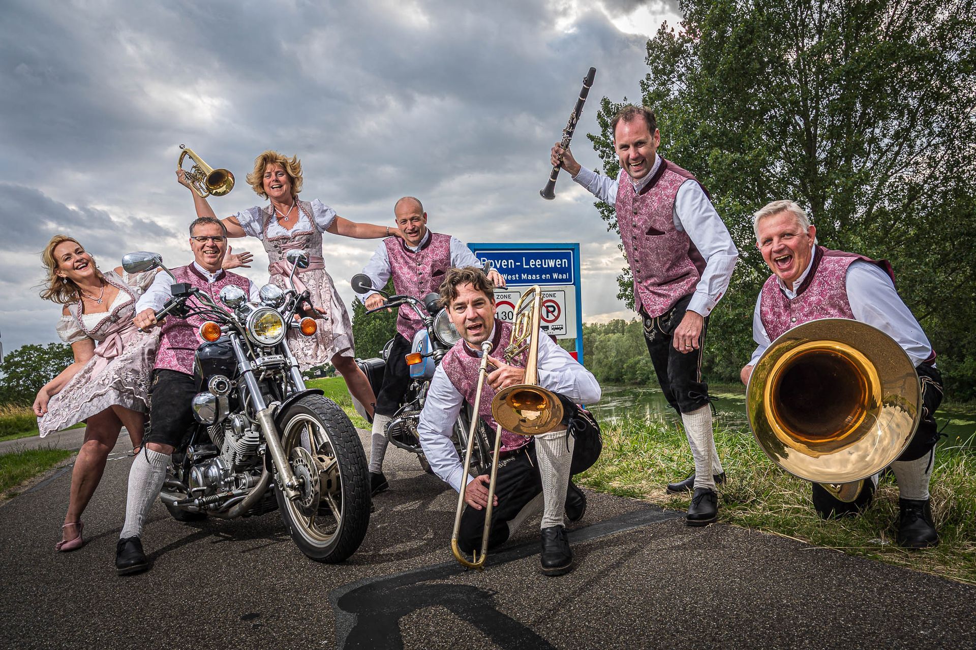 Een groep mensen poseert voor een foto met motorfietsen en koperblaasinstrumenten.