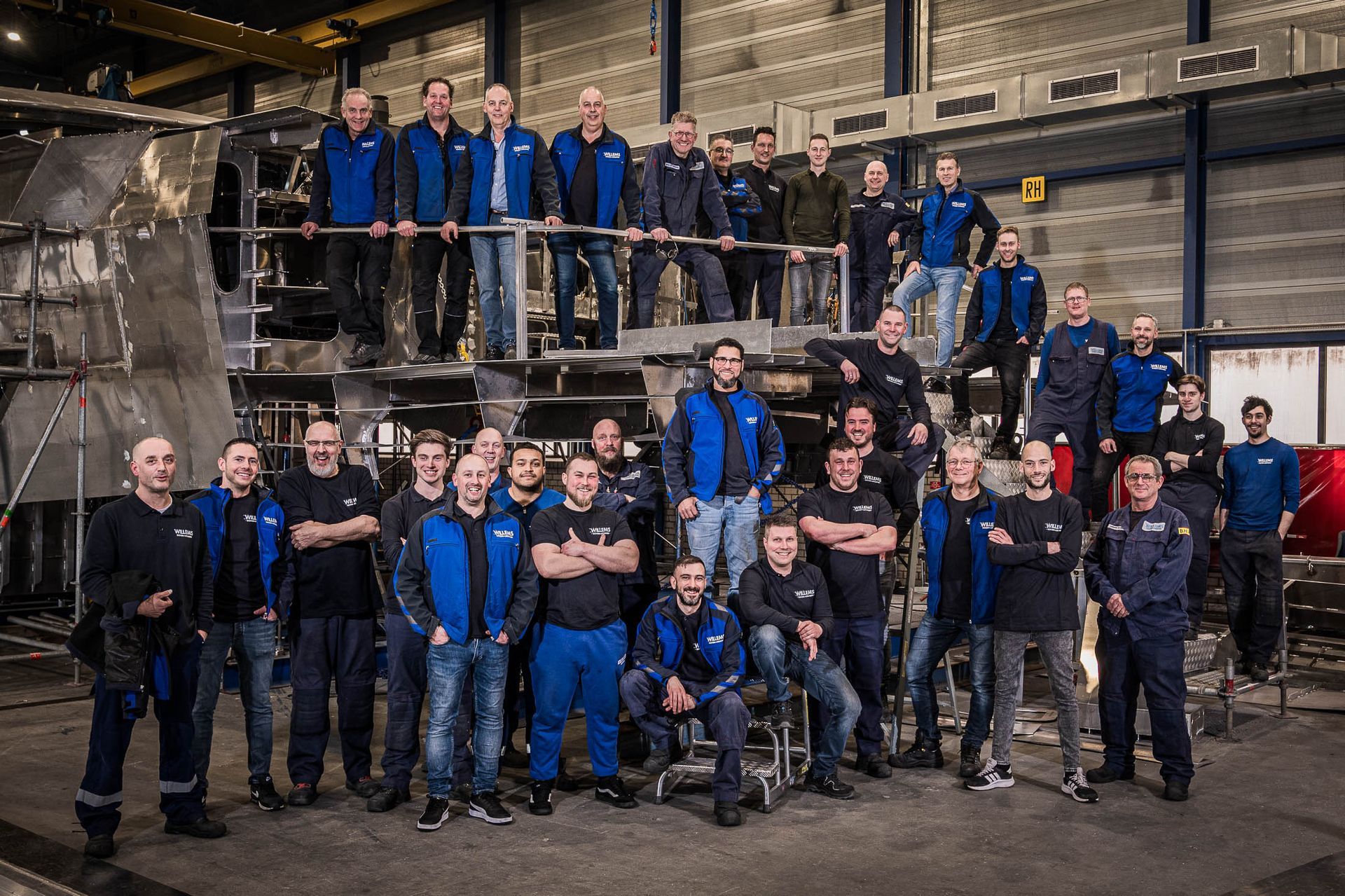 Een grote groep mannen poseert voor een foto in een fabriek.