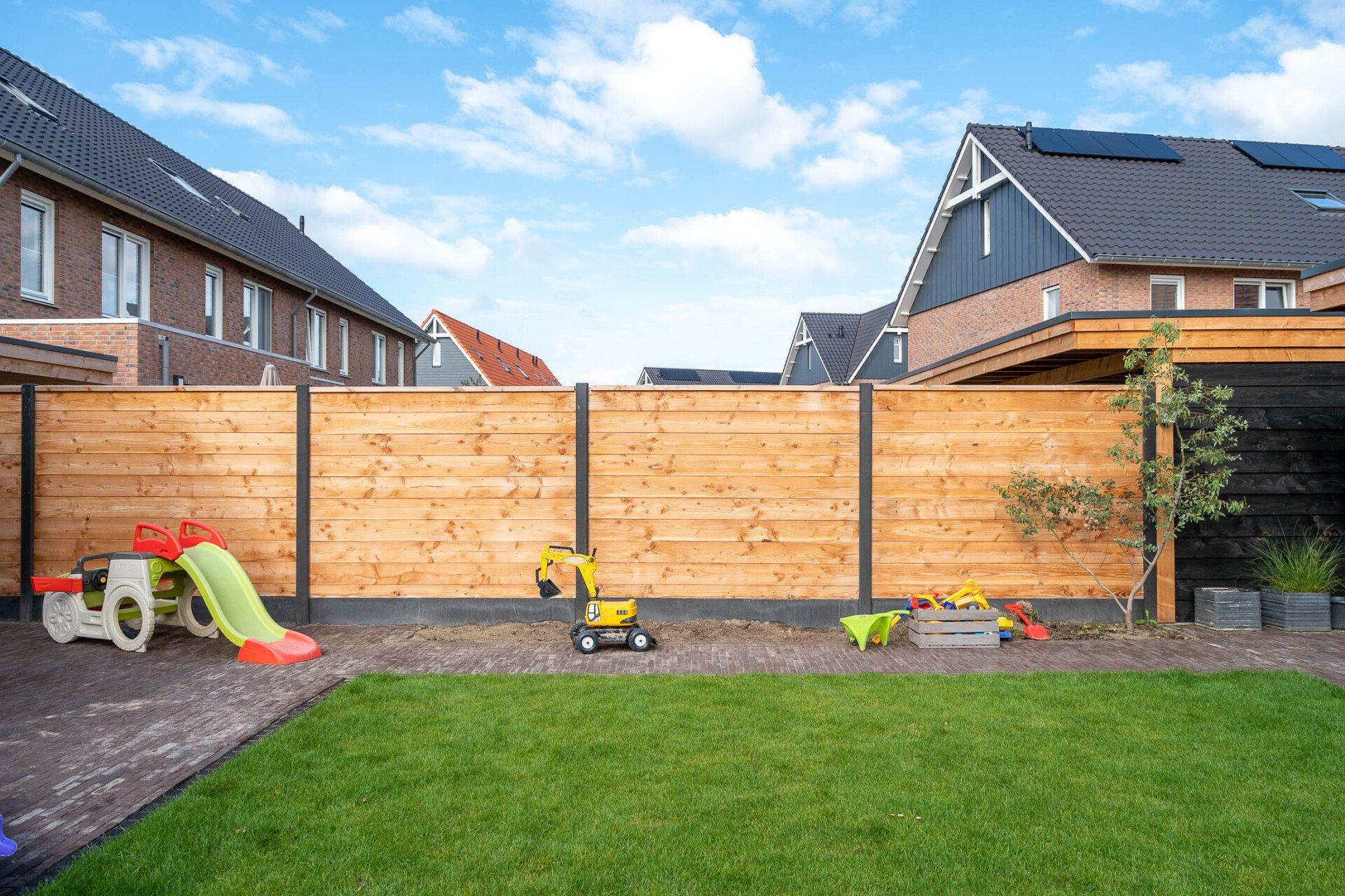 Een achtertuin met een houten hek en een speeltuin voor een huis.