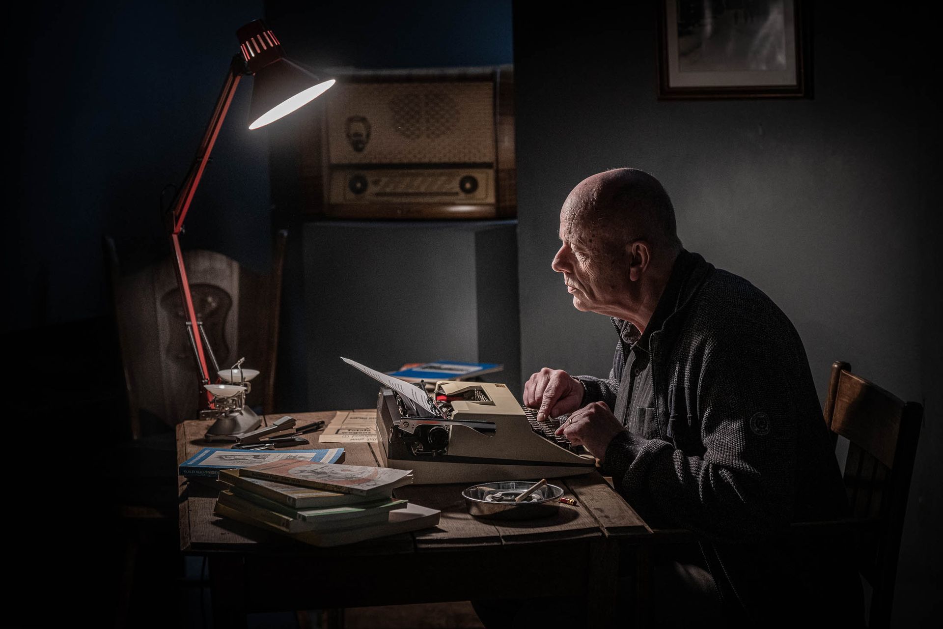 Een oudere man zit aan een tafel met een lamp.