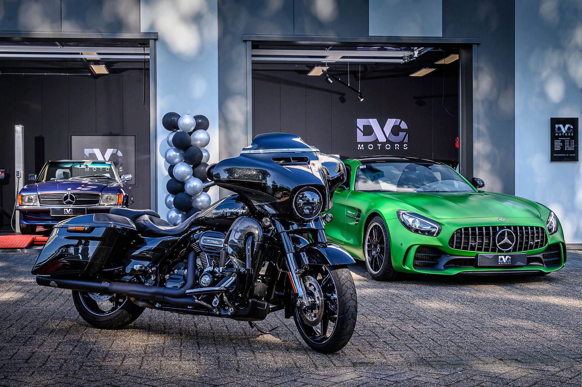 Een motor en een groene auto staan voor een garage geparkeerd.