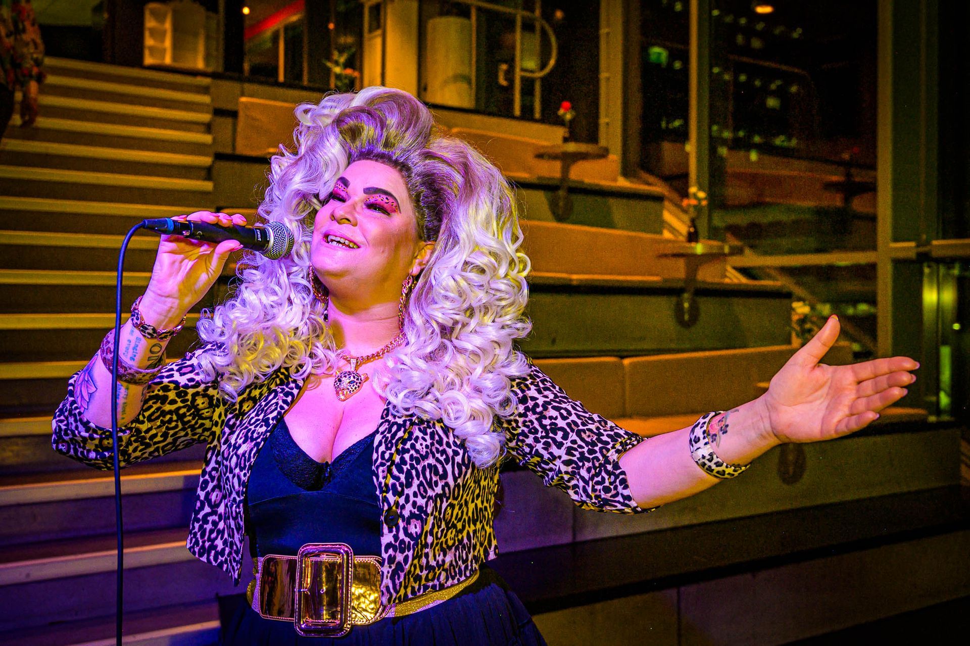 Een vrouw met een pruik zingt in een microfoon.