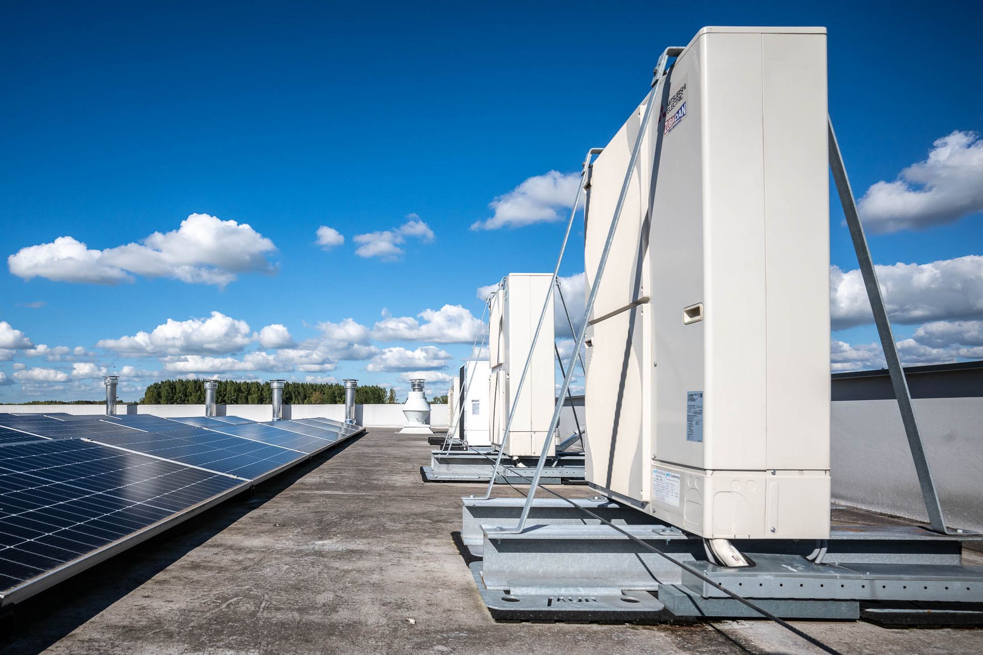 Een rij witte dozen staat op een dak naast zonnepanelen.