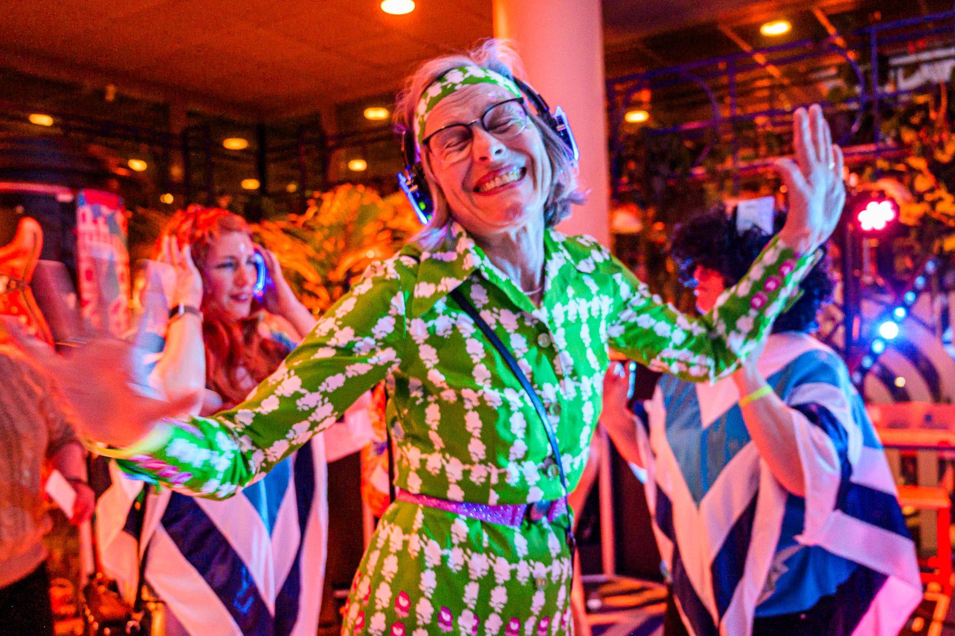 Een vrouw in een groene jurk en haarband danst op een feestje.