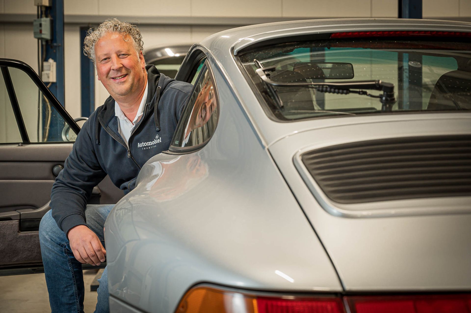 Een man zit achterop een zilveren auto.
