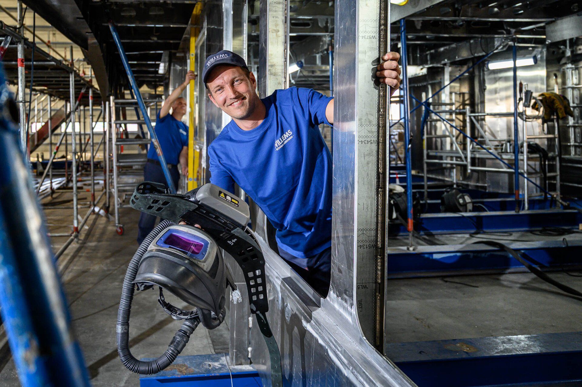 Een man in een blauw shirt staat naast een machine in een fabriek.