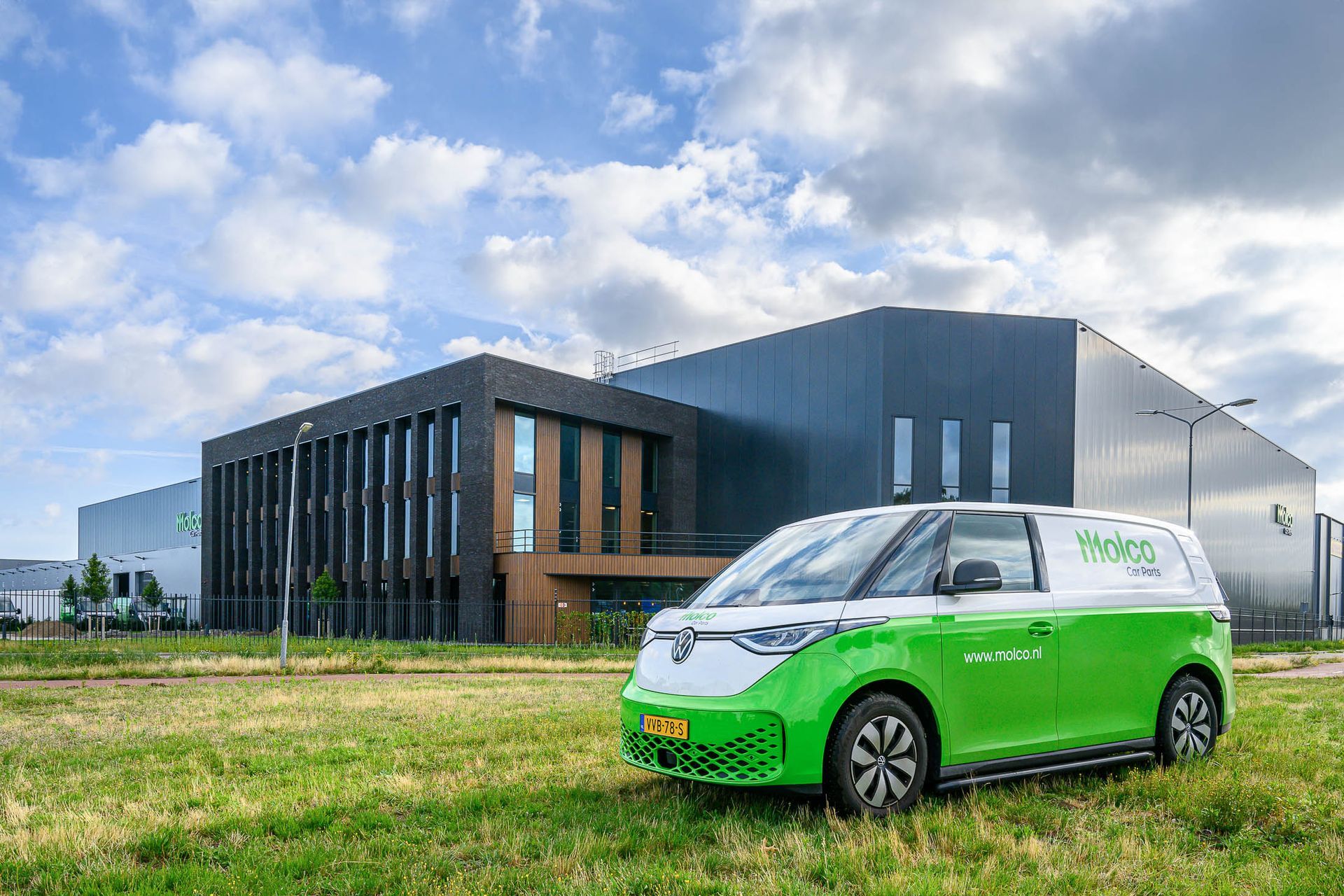 Een groen-wit busje staat geparkeerd voor een groot gebouw.