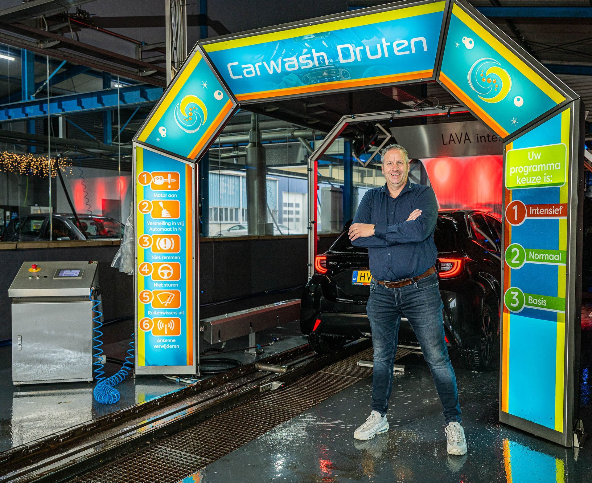 Een man staat bij de ingang van een autowasstraat. Op het bord staat