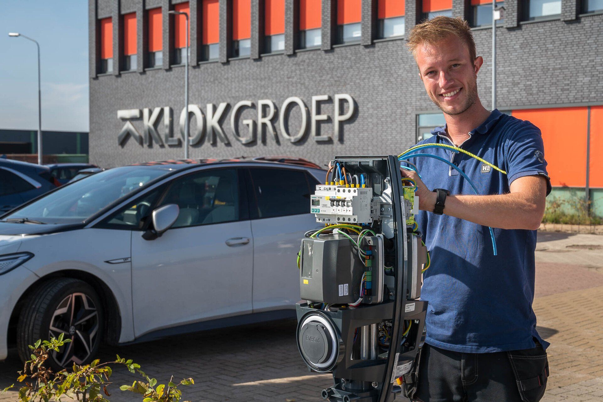 Een man staat voor een witte auto en houdt een apparaat vast.