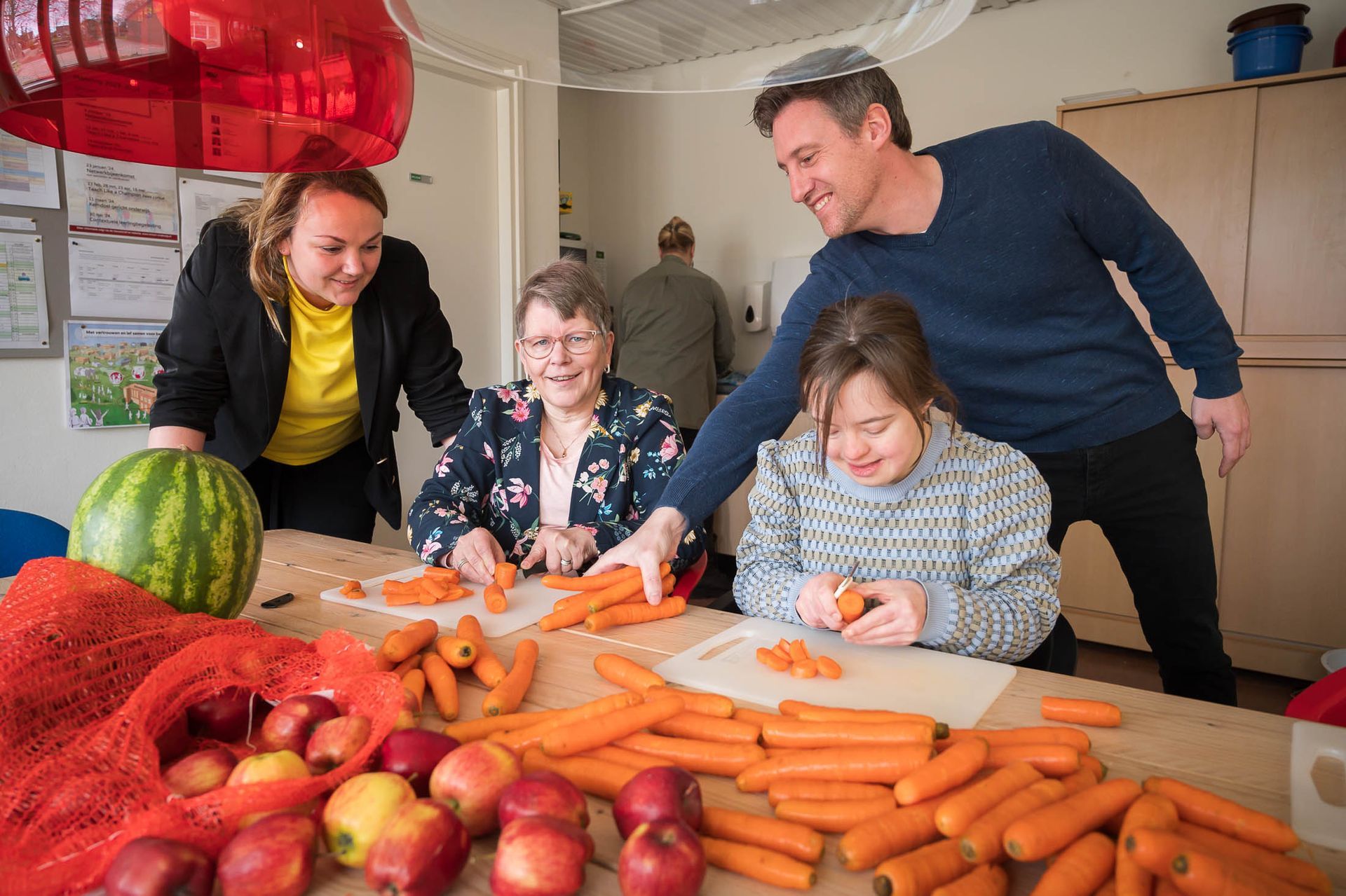 Een groep mensen zit rond een tafel wortels te snijden.
