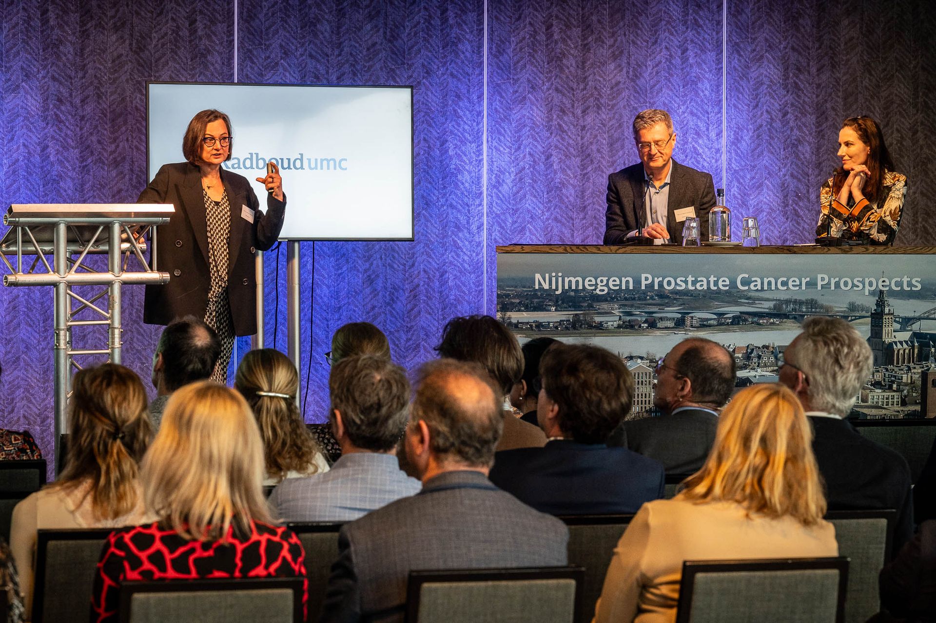 Een vrouw geeft een presentatie aan een groep mensen op een conferentie.